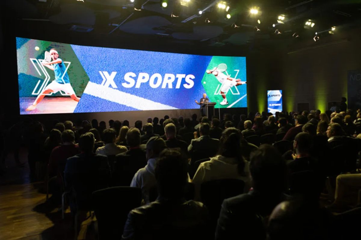 Telão com o logo do Xsports em um auditório