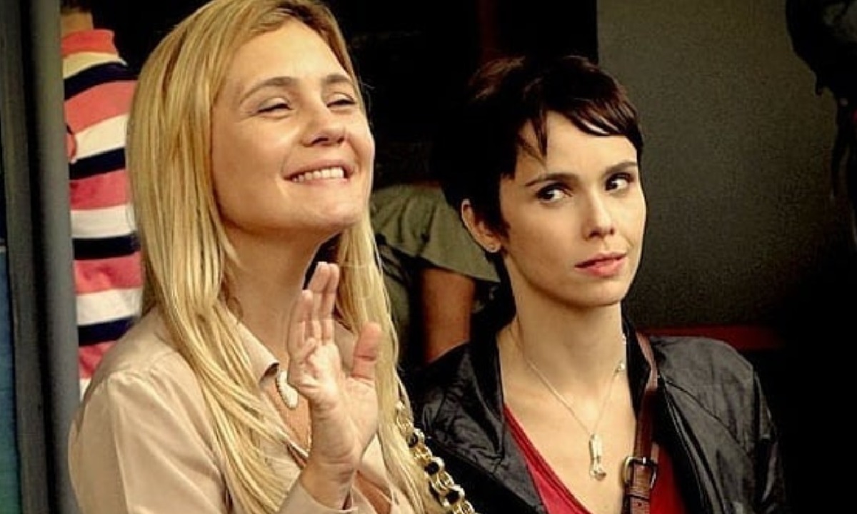 Atrizes Deborah Secco e Maria Fernanda Cândido em cena de novela. Deborah Secco sorri e gesticula com a mão.
