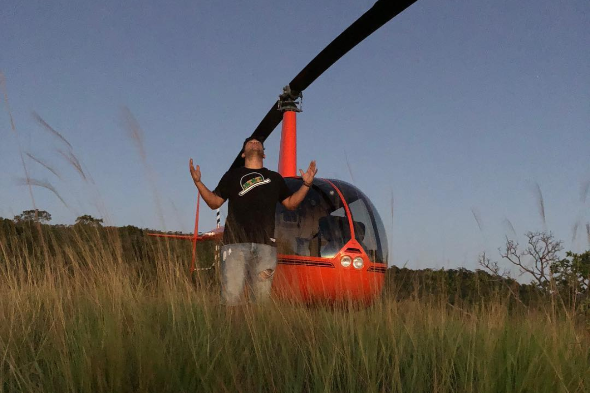 Henrique, da dupla com Juliano, ajoelhado com um helicóptero atrás