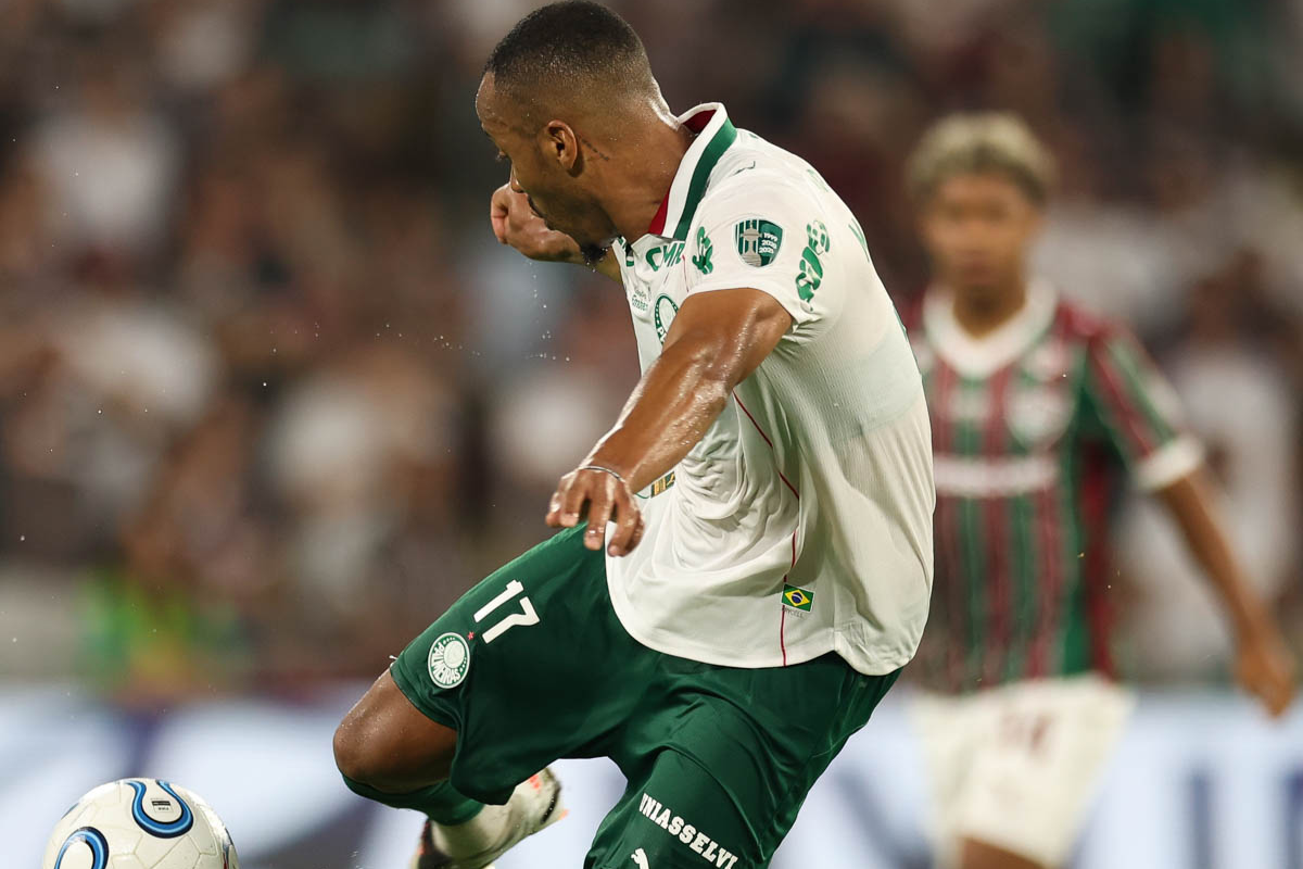 Jogador do Palmeiras indo chutar a bola enquanto atleta do Fluminense observa