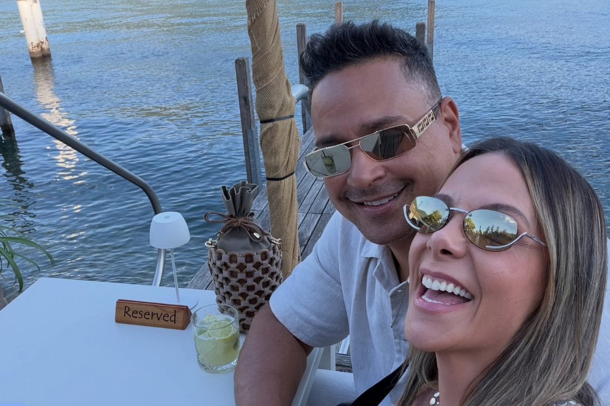 Carla Perez e Xanddy rindo, com paisagem de um mar